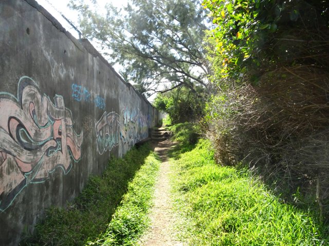 Le sentier le long du mur en direction du petit supermarché